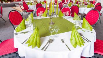 A round dining table with white tablecloth, green napkins, and red chairs.