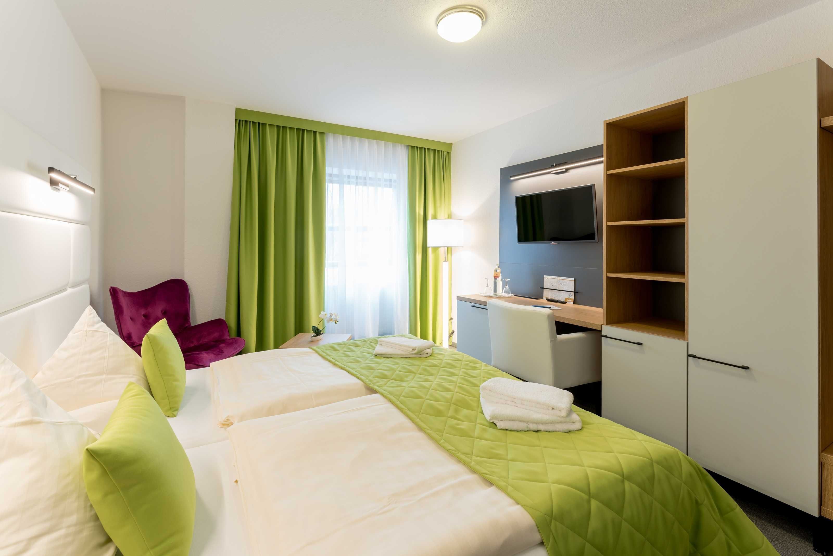 A hotel room with two beds, a desk, a television, and a wardrobe.