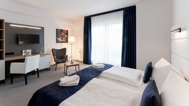 Une chambre d’hôtel avec deux lits, un bureau, une chaise, une télévision et une grande fenêtre avec des rideaux.