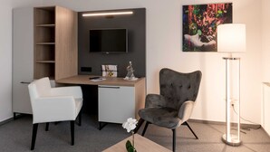 Une chambre d’hôtel moderne équipée d’un bureau, de deux chaises, d’une télévision, d’un tableau et d’une lampe sur pied.