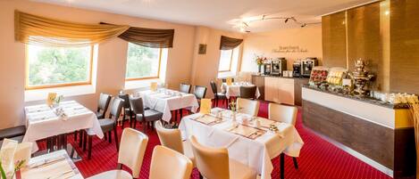 Un restaurant avec des tables dressées pour le service, un bar et une vue sur l’extérieur.