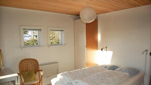 Quarto com cama, cadeira, duas janelas, radiador e luminária pendente.