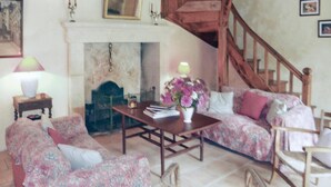 Una sala acogedora con chimenea, sofá floral y una escalera.