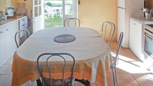 Un comedor con una mesa dispuesta para cuatro personas, rodeada de sillas de metal. A la derecha, hay un refrigerador y una estufa en la cocina.