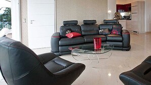 Un salon avec un canapé en cuir noir, une table basse en verre et un coin repas comprenant une table et des chaises en bois.