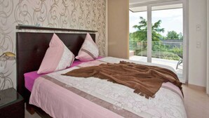 Une chambre à coucher avec un lit, des oreillers, une couverture, une table de chevet et une fenêtre donnant sur un paysage verdoyant.