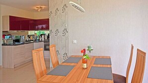 Un coin repas avec une table et des chaises en bois, un vase rempli de fleurs et, au fond, une cuisine.