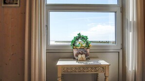 Ein Fenster mit Blick auf den Strand und Zelte, ein kleiner Tisch mit einem dekorativen Gegenstand sowie Holzvertäfelung an der Wand.
