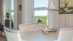 Ein Essbereich mit einem weißen Tisch, Korbstühlen, einem Blumenkorb und einem Bild an der Wand.