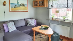 A cozy living room with a grey sofa, a wooden coffee table, and a window with a view of a red building.