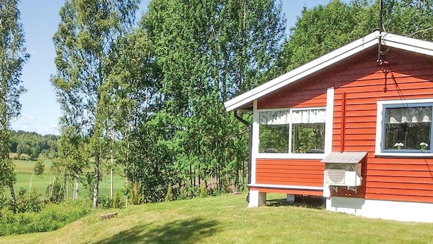 A red and white cabin with a small porch, surrounded by a lush green landscape and tall trees.