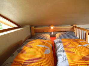 A small, cozy room with two beds, a wooden headboard, and a window providing natural light.