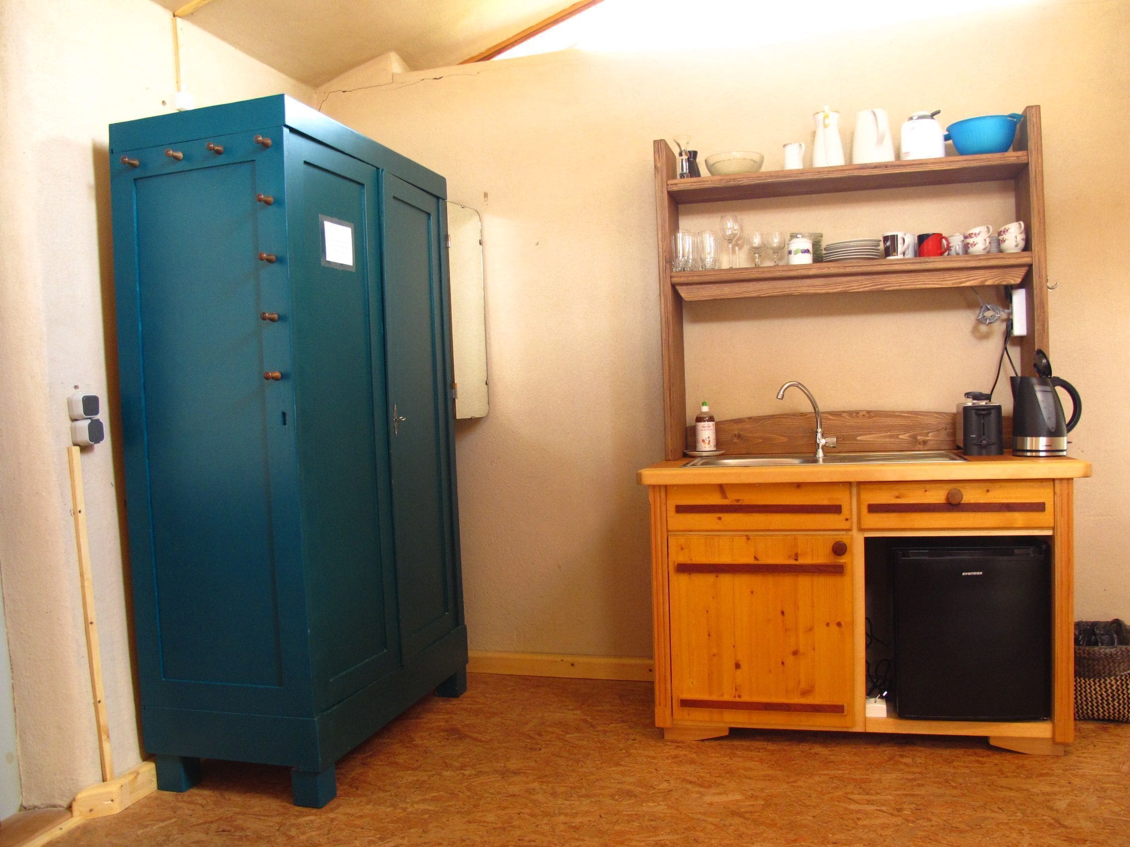 A compact kitchen with a sink, a small refrigerator, and a shelf with kitchenware.