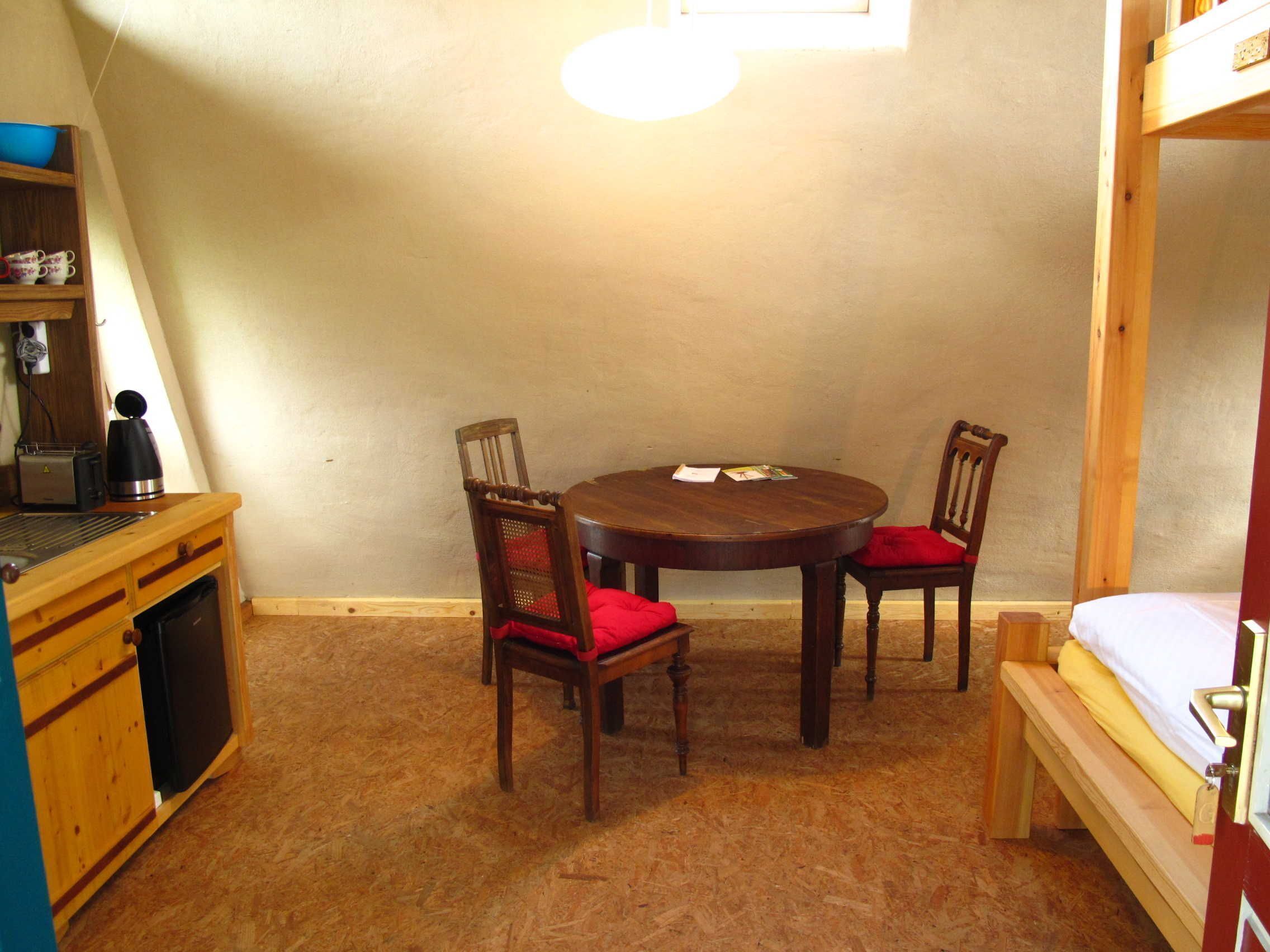 A compact room with a round wooden table and two chairs, a small kitchenette, and a bunk bed.