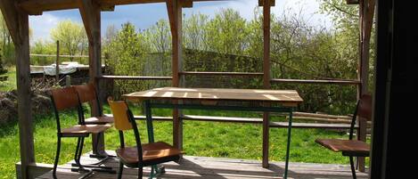 A covered outdoor area with a table and chairs, solar panels on the roof, and a view of trees and grass.