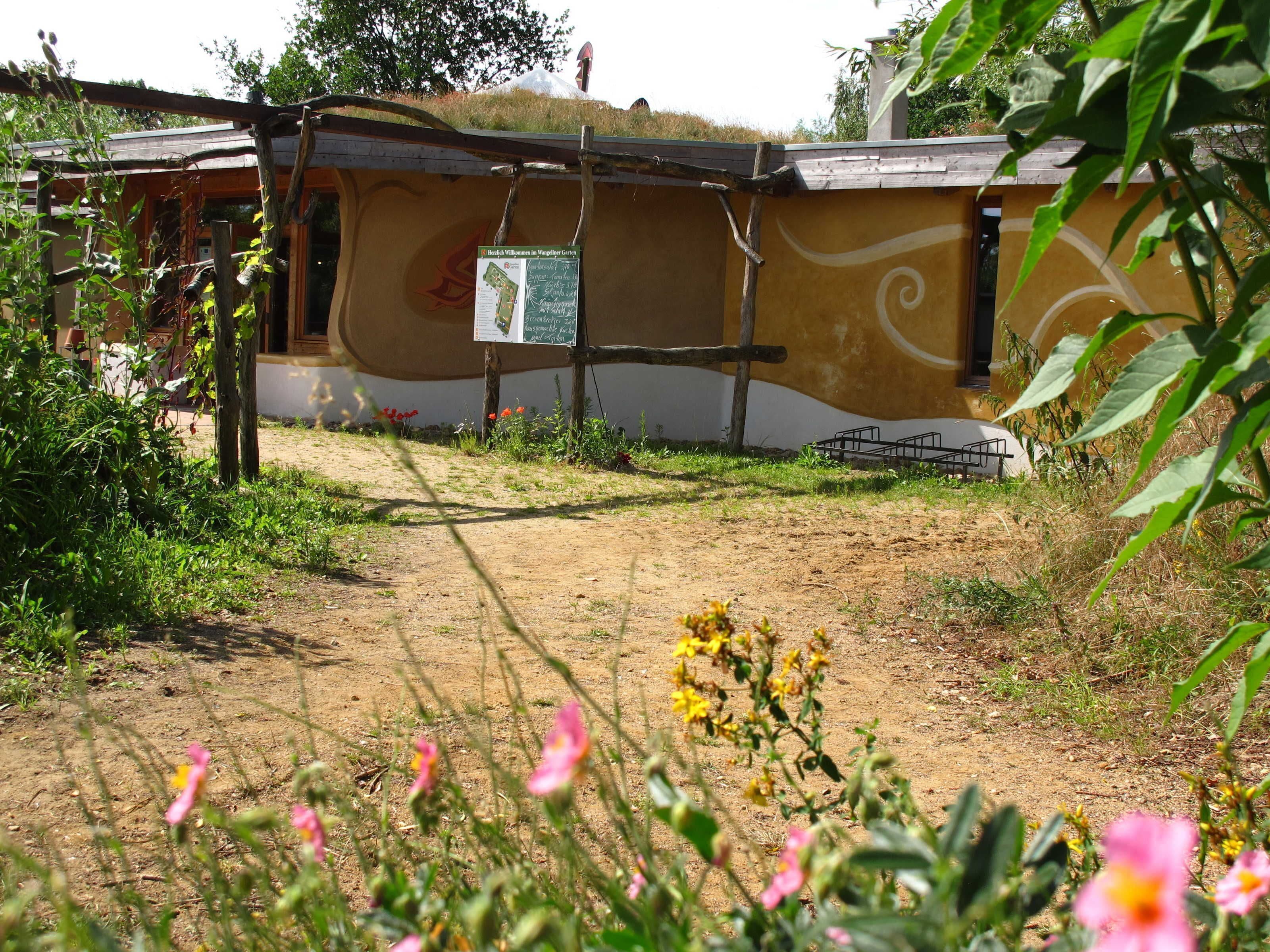 Un edificio con una pared exterior curva distintiva, un cartel y un camino de tierra que conduce a él.