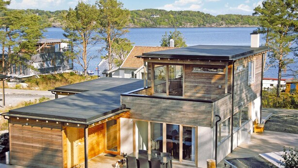 Een modern huis met twee verdiepingen, een overdekte patio en uitzicht op een meer.