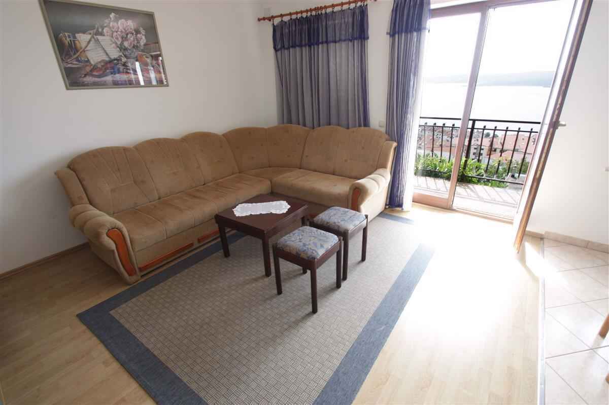 Un soggiorno con un divano angolare beige, due poltrone abbinate, un tavolino da caffè e vista sul mare da un balcone.