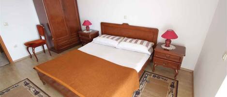 A bedroom with a large bed, two bedside tables with lamps, a wardrobe, and a rug.