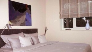 A bedroom with a bed, a nightstand, a lamp, a window with a curtain, and a painting on the wall.