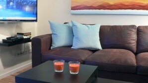 A living room with a brown sofa, two light blue pillows, a flat-screen TV, and a coffee table with two glasses of orange drink.