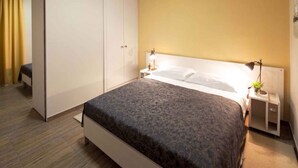 Une chambre d’hôtel bien aménagée, avec un grand lit, une armoire et une table de chevet dotée d’une lampe.
