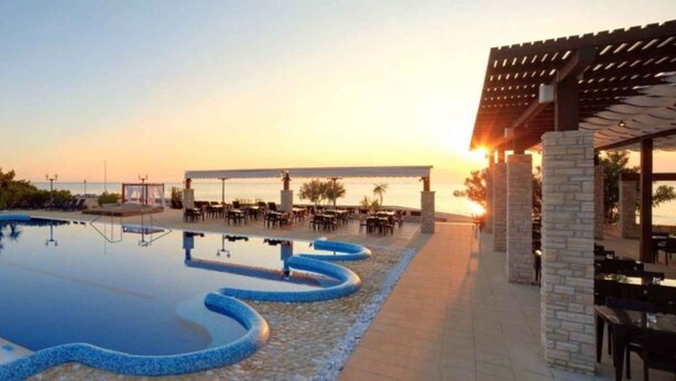 Une piscine à débordement, entourée d’une terrasse aménagée avec des sièges d’extérieur et offrant une vue sur le coucher du soleil.