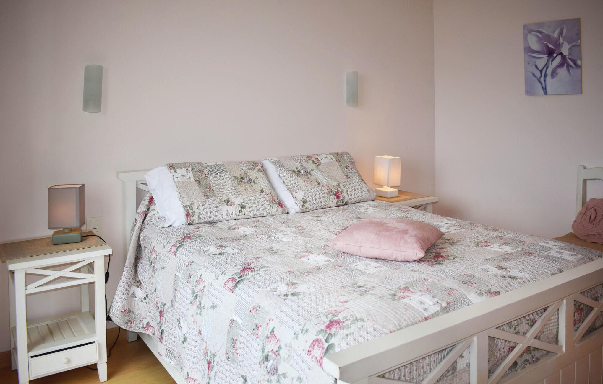 A bedroom with a floral bedspread, a bedside lamp, and a nightstand with a lamp.