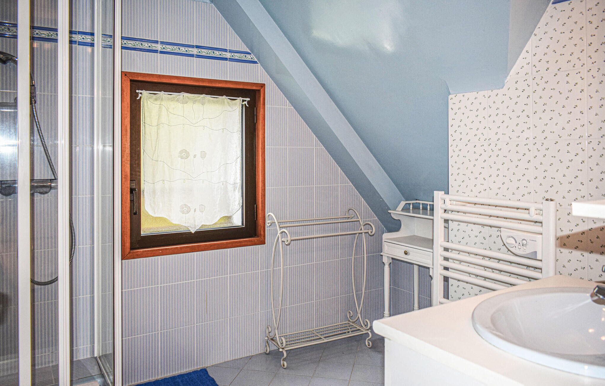 Een badkamer met een douche, een raam met gordijn, een radiator en een wastafel.