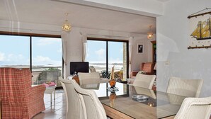 Amplia sala de estar con una gran mesa de vidrio rodeada de sillas de mimbre, un televisor y un modelo de velero.