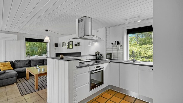 Een moderne keuken met witte kastjes, een ingebouwde oven en een magnetron. Er is een zithoek met een grijze bank en een kleine tafel.