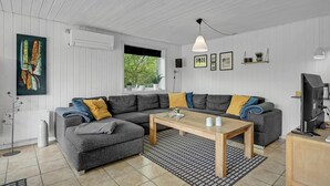 Een moderne woonkamer met een grijze hoekbank, een houten salontafel en een kamerkleed met een patroon.
