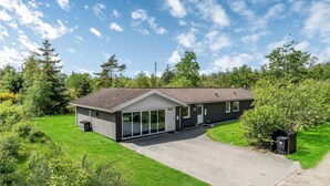 Een modern huis met twee verdiepingen, een schuin dak, grote ramen en een geplaveid pad.