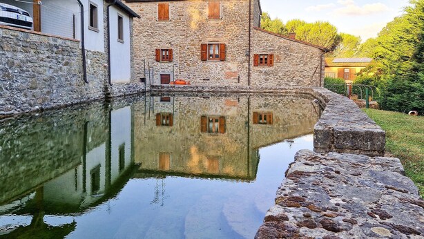 Un edificio de piedra reflejado en aguas tranquilas, rodeado de vegetación.