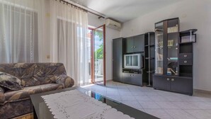 A living room with a sofa, a glass coffee table with a white doily, a television, and a black cabinet with glass doors. - Holiday apartment with air conditioning and WLAN (Crikvenica)