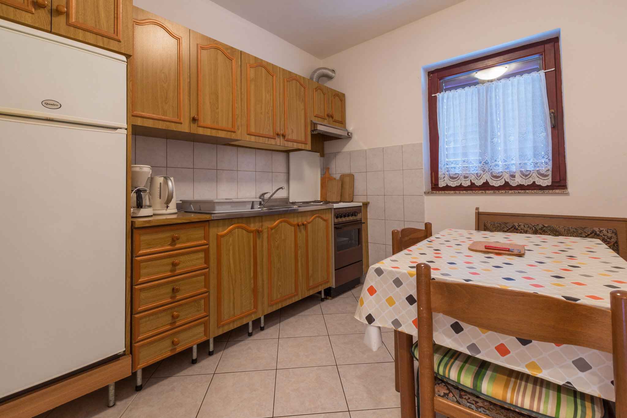 Eine kleine Küche mit Holzausbau, einem weißen Kühlschrank, einem Herd und einem Esstisch mit bunten Tischdecken.