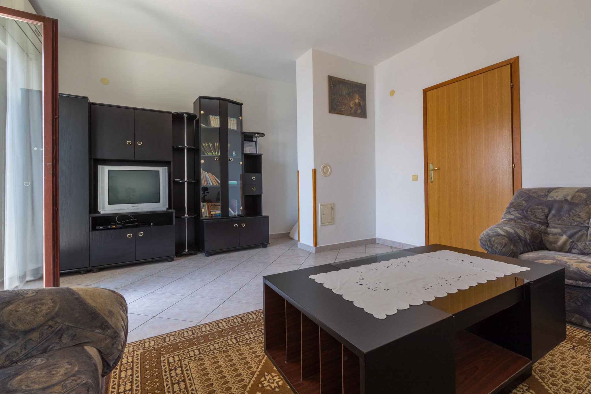 Una sala de estar con un sofá, una mesa de centro, un televisor y un mueble con estantes.