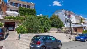 A residential street with parked cars, a building with a satellite dish, and a clear blue sky. - Holiday apartment with air conditioning and WLAN (Crikvenica)