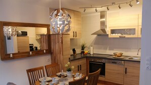 A modern kitchen with wooden cabinets, a dining table set for four, and a large mirror above the counter. - Apartment Bergblüte - FeWo (Bad Harzburg)