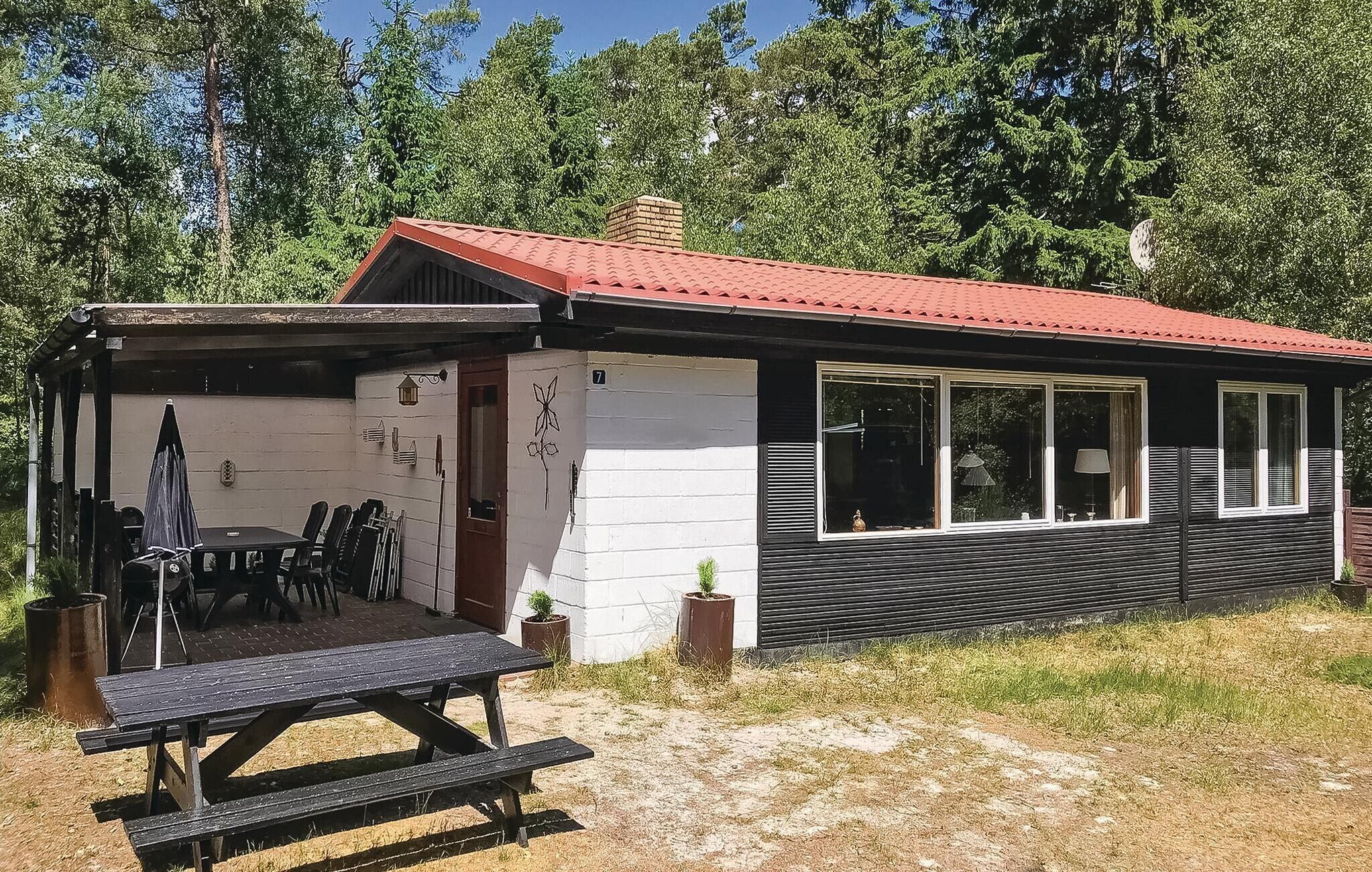 A cabin with a red roof, a covered patio with a table and chairs, and a small garden area.