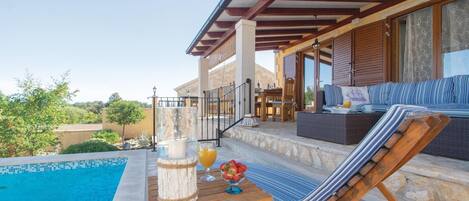 A poolside area with a lounge chair, a table with a drink and fruit, and a view of the pool.