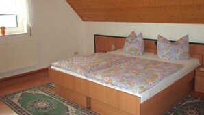 A bedroom with a wooden ceiling, a bed with floral bedding, and a window with curtains. - Kräuter-Landhaus, Germany (Bad Schmiedeberg)
