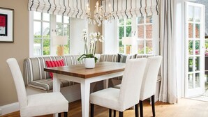 A dining area with a wooden table, white upholstered chairs, a striped bench, and a chandelier.
