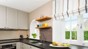 A modern kitchen with white cabinets, a black countertop, a built-in oven, a sink, and a window with a view of greenery.