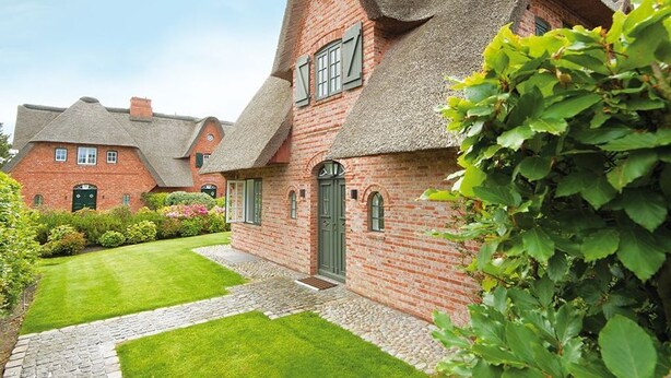 A traditional brick house with a thatched roof and a well-maintained garden.