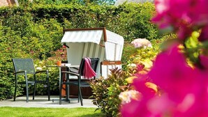 A garden with a white outdoor seating area, including a table and chairs, surrounded by lush greenery and flowering plants.