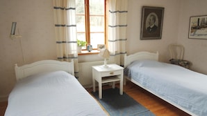A bedroom with two single beds, a bedside table with a lamp, a window with curtains, a radiator, and a framed picture on the wall. - 3 bedroom nice home in Tranås (Tranås)