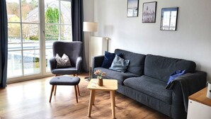 A modern living room with a grey sofa, a grey armchair, a wooden coffee table, and a floor lamp. There are three framed pictures on the wall. - (171) 3- room apartment - apartment house Strandstr. 16 (Kühlungsborn)
