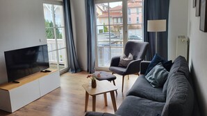 A modern living room with a flat-screen TV, grey sofa, armchair, and a small wooden coffee table. - (171) 3- room apartment - apartment house Strandstr. 16 (Kühlungsborn)
