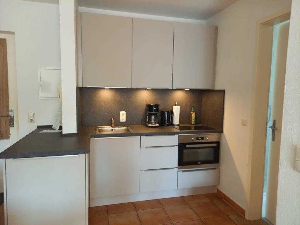 A compact kitchen with white cabinets, a black countertop, a coffee maker, a kettle, and an oven.